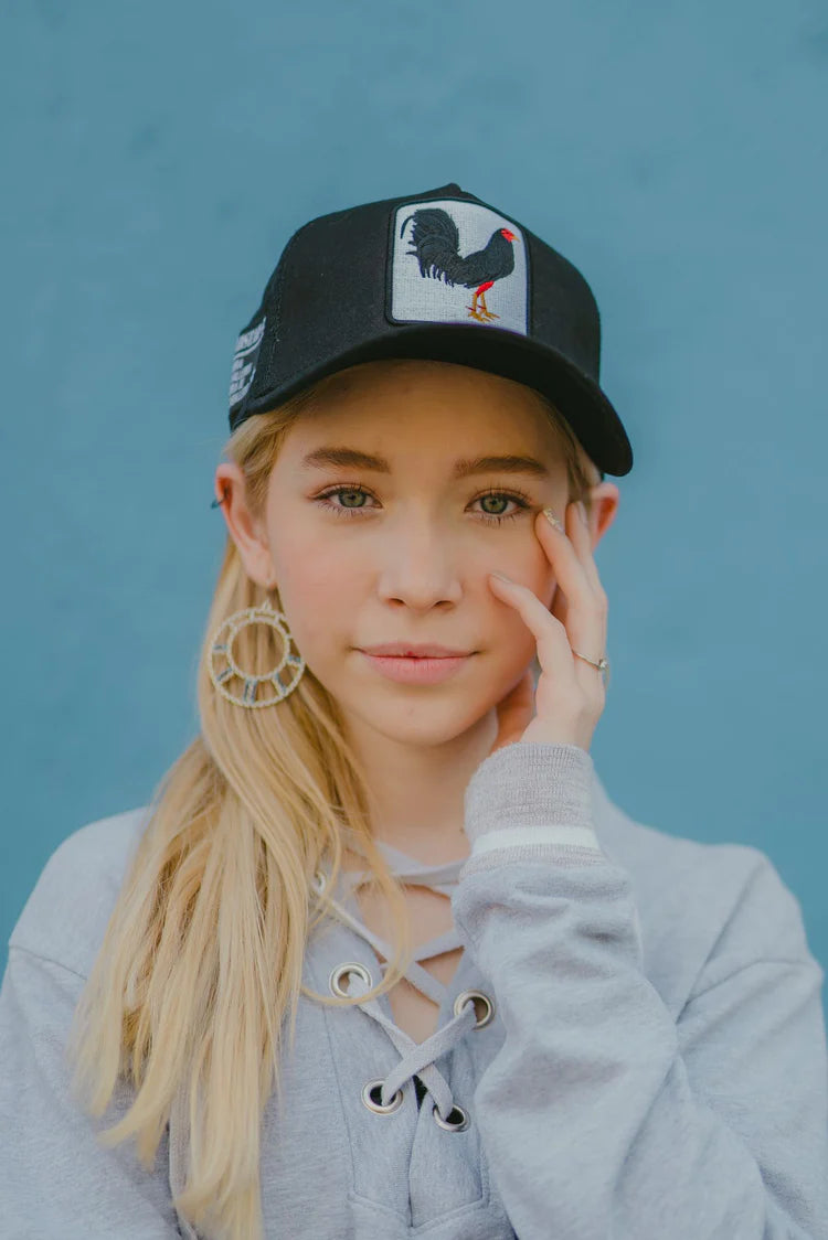 Front view of a woman wearing the Gold Star Rooster Black Trucker Hat, demonstrating the unisex design and stylish fit