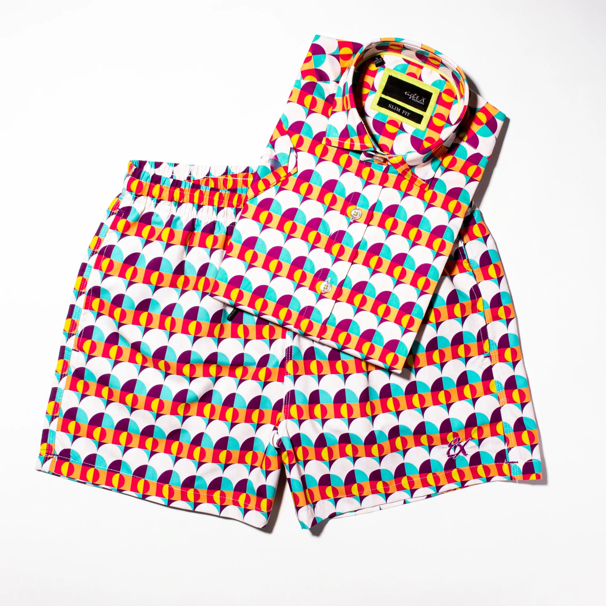 Sunset Alchemy Swim Trunks kept with the matching Sunset Alchemy Short Sleeve Shirt folded, highlighting their vibrant colors and stylish design, perfect for a coordinated summer outfit